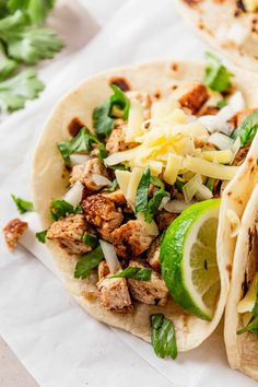 two tacos with meat, cheese and vegetables on them sitting on a piece of paper