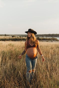 a pregnant woman in a cowboy hat walks through tall grass