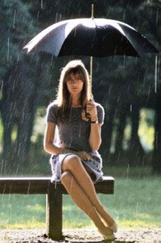 a woman sitting on a bench in the rain holding an umbrella and looking at the camera