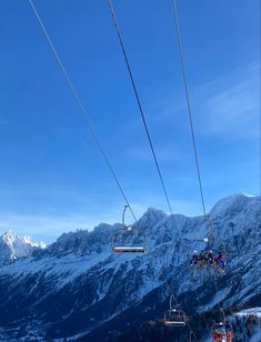 two people riding on a ski lift above the snow covered mountain range, with mountains in the background