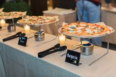 three pizzas on trays sitting on top of a table with candles in front of them