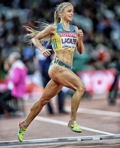 a woman running on a track with people watching from the sidelines behind her and in the background