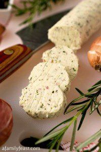 several different types of cheese on a cutting board next to onion and garlic sticks with rosemary sprigs in the background