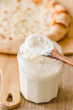 a wooden spoon full of whipped cream next to a pizza