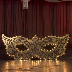 a masquerade mask sitting on the floor with lights around it and a chandelier hanging from the ceiling