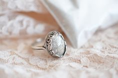 a ring sitting on top of a white lace covered table cloth next to a pillow