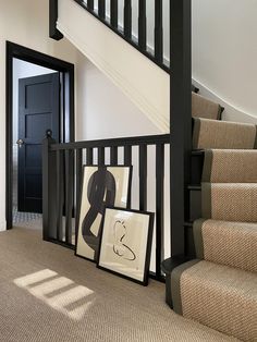 an entryway with stairs and pictures on the floor next to it in front of a black door