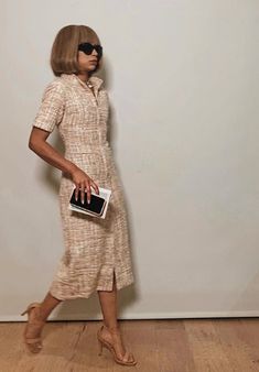 a woman is standing in front of a white wall holding a black and white purse