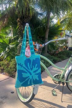 a green bicycle with a blue bag on the front wheel and palm trees in the background