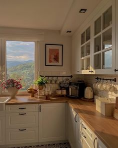 a kitchen with white cabinets and wooden counter tops next to a window overlooking the mountains