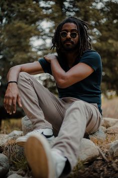 a man with dreadlocks sitting on top of a rock next to trees and rocks