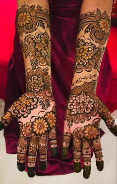 two hands with henna tattoos on them, one is showing the intricate design and the other has flowers