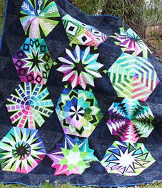 a colorful quilt on the grass with trees in the background