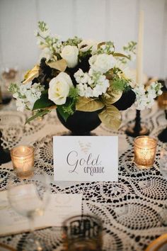 a table topped with a vase filled with white flowers and greenery next to candles