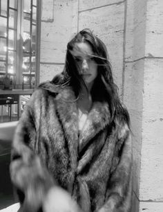 black and white photograph of woman in fur coat walking down the street with her hand on her hip