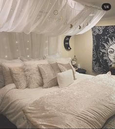 a white bed with lots of pillows on top of it next to a curtained window