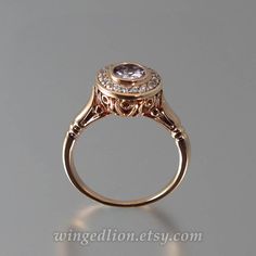 The SECRET DELIGHT engagement ring will be custom made in 14K rose gold in the size specified by the customer. The SECRET DELIGHT has clean lines, contemporary well-defined shapes, and intricate carvings. From the top, the ring looks like a traditional halo ring. The brilliant halo contains 19 genuine white diamonds (VS, 1.5mm, approximate total carat weight 0.28ct). The central gem is a natural 6.2mm Spinel (1.02ct, VVS - eye clean). Spinel is quite a remarkable stone that comes in a wide range Luxury 14k Rose Gold Halo Setting Rings, Luxury 14k Rose Gold Rings With Halo Setting, 14k Rose Gold Halo Ring, Formal Rose Gold Halo Setting Wedding Ring, Elegant 14k Rose Gold Diamond Ring With Bezel Setting, Elegant 14k Rose Gold Ring With Halo Design, 14k Rose Gold Halo Diamond Ring For Wedding, 14k Rose Gold Halo Wedding Ring, Elegant Rose Gold Diamond Ring With Halo Setting