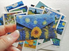 a hand holding a blue envelope with yellow flowers on it and many pictures around it