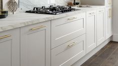 a white kitchen with marble counter tops and gold pulls on the cabinet doors is shown