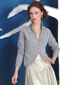 a woman standing in front of a blue background wearing a silver skirt and cardigan