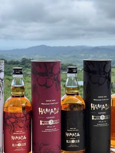 four bottles of various types of alcohol are lined up on a table with mountains in the background