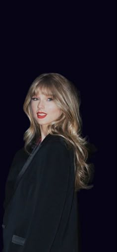 a woman with long blonde hair wearing a black suit and red lipstick in front of a dark background