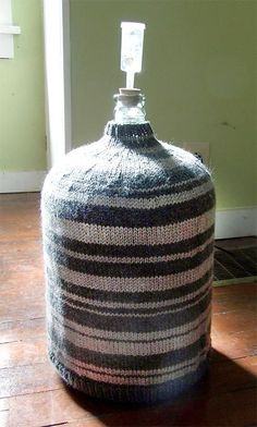 a knitted bottle sitting on top of a wooden floor next to a wall and door