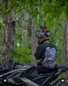 a man sitting on top of a motorcycle in the forest talking on his cell phone