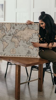 a woman is sitting on a bench looking at a large world map that she made