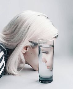 a woman with her head down next to a glass filled with water and the image of a man's face is reflected in it