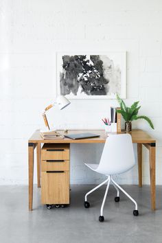 a white chair sitting next to a desk with a laptop on it and a plant in the corner