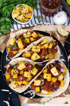 three tacos with meat and pineapple salsa on a black plate next to limes