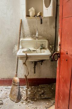 an old sink and broom in a run down bathroom