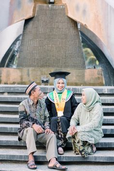 three people sitting on the steps in front of a fountain wearing graduation caps and gowns