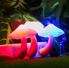 two small figurines stand next to mushrooms in the grass with plants behind them