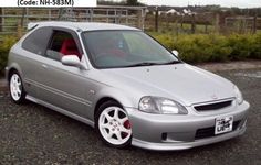 a silver car parked in front of a fenced area with grass and bushes behind it