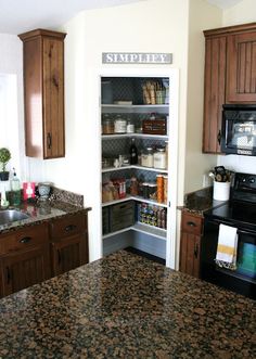 a kitchen with brown cabinets and granite counter tops, an open pantry door is visible