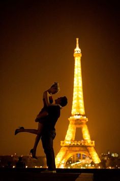 a man and woman are kissing in front of the eiffel tower at night