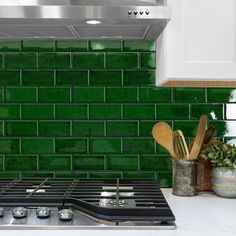 a stove top oven sitting next to a green tile backsplash in a kitchen