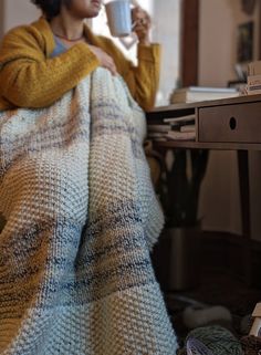 a woman sitting on a couch holding a coffee cup in her hand while wrapped in a blanket