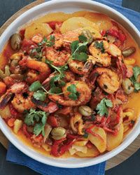 a white bowl filled with pasta and shrimp on top of a blue cloth next to a wooden cutting board