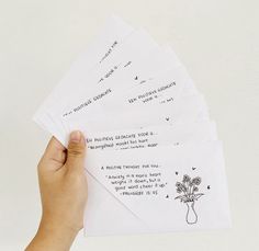 a hand holding five envelopes with writing on them and flowers in a vase next to it