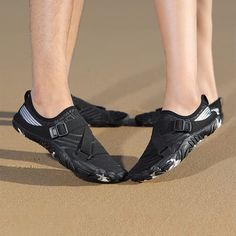 a man standing on top of a sandy beach next to the ocean wearing black shoes