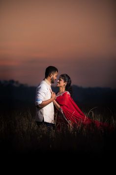 a man and woman standing in the middle of a field at sunset