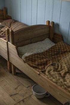 two wooden beds in a room with blue walls and wood flooring, one has a brown checkered blanket on it