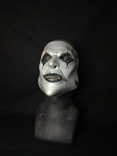 a white mask with black and silver paint on it's face is shown against a black background