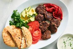 a white plate topped with meatballs, tomatoes and cucumbers next to a bowl of ranch dressing