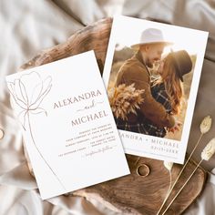 two wedding cards sitting on top of a piece of wood next to dried flowers and leaves