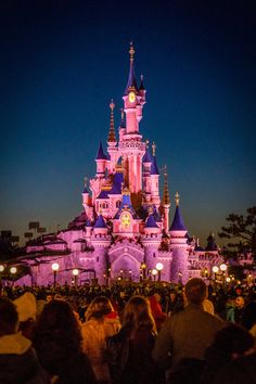 the castle is lit up at night with people standing in front and looking around it