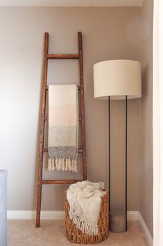 a ladder leaning against the wall next to a basket with a blanket on it and a lamp